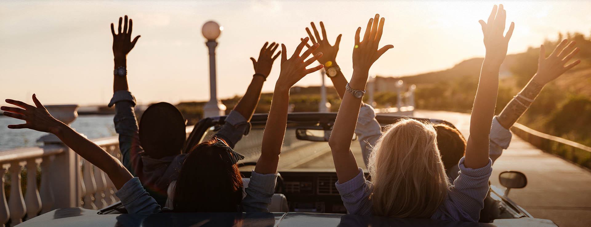 Menschen mit erhobenen Armen in einem Cabrio bei Sonnenuntergang