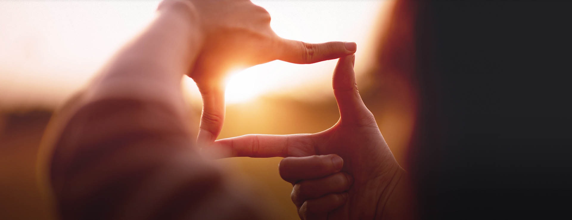 Hände formen einen Kreis vor einem Sonnenuntergang